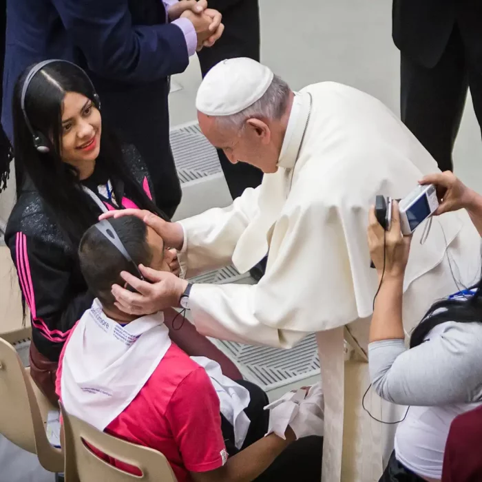 Pope Francis speaking with an individual in a crowd.